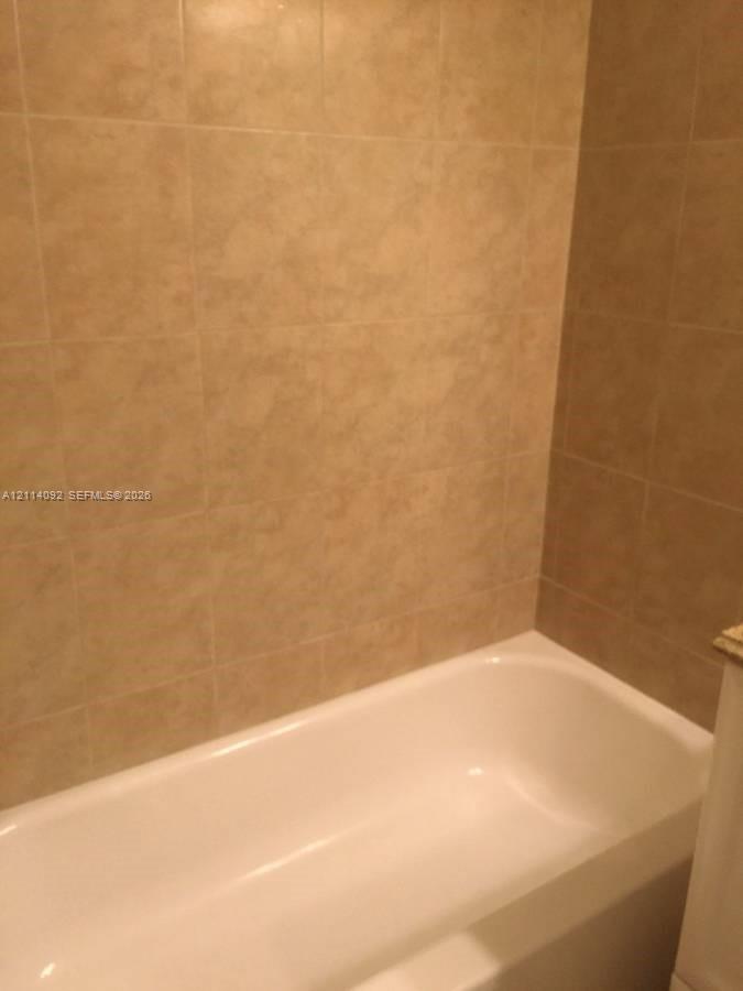 Bathtub featuring a white finish and full-height, square-format stone-tile surround