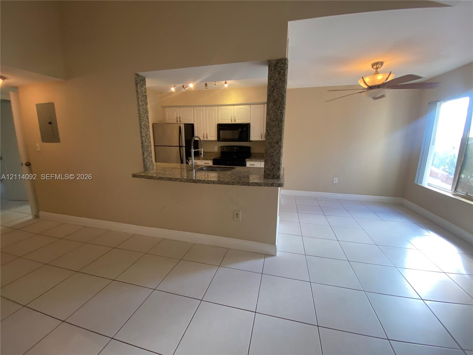 Kitchen featuring a stone-topped breakfast bar, white cabinetry, integrated stainless steel appliances, tile flooring, and a ceiling fan with light fixture