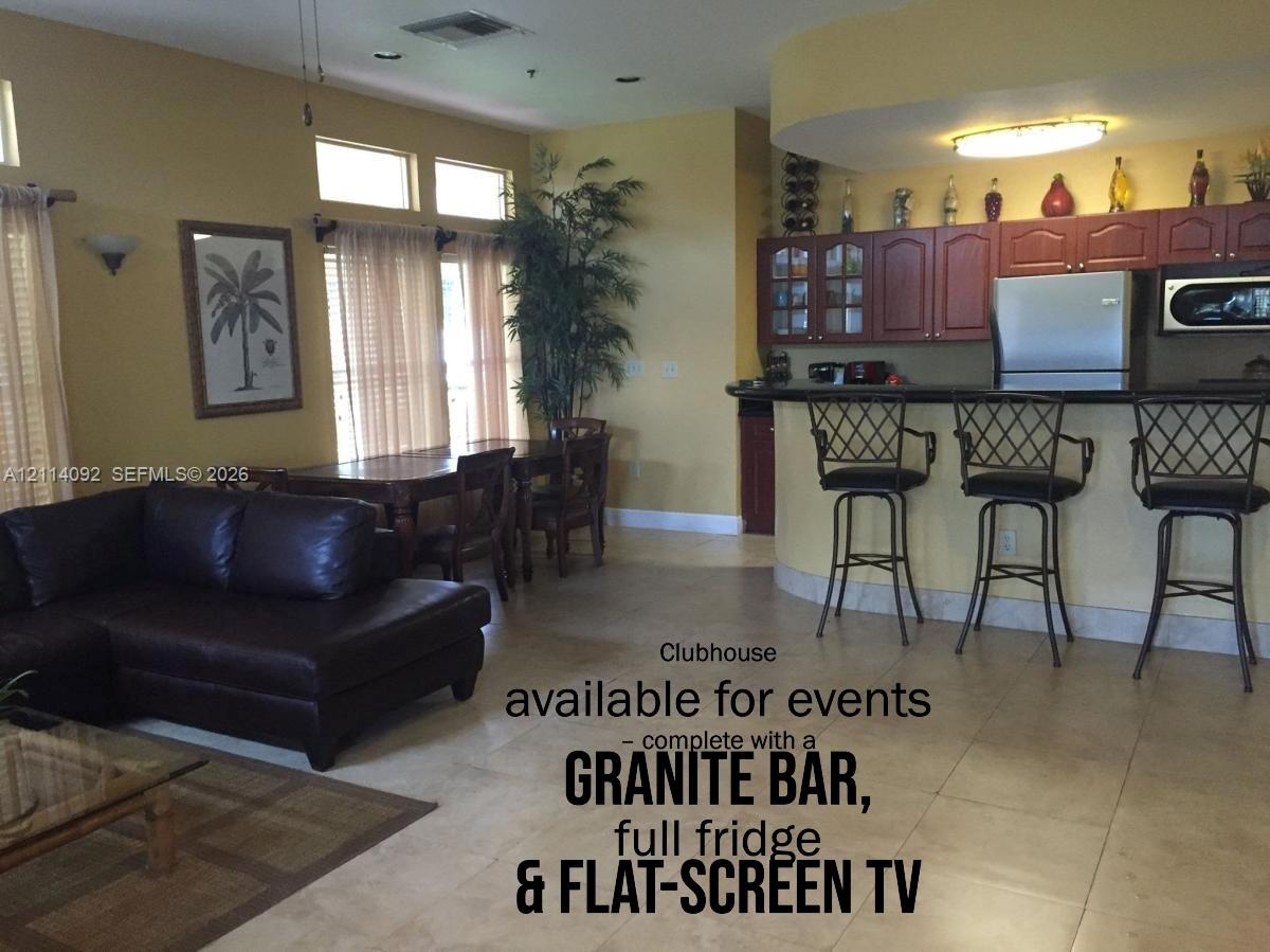 Common area featuring stone-surfaced bar with stainless steel refrigerator, built-in cabinetry, and tile flooring