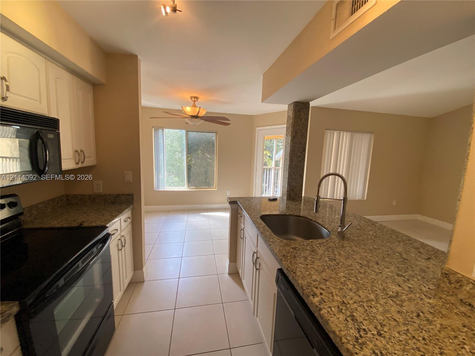 Kitchen featuring stone countertops, white cabinetry, tile flooring, an undermount stainless steel sink with a goose-neck faucet, and built-in black appliances