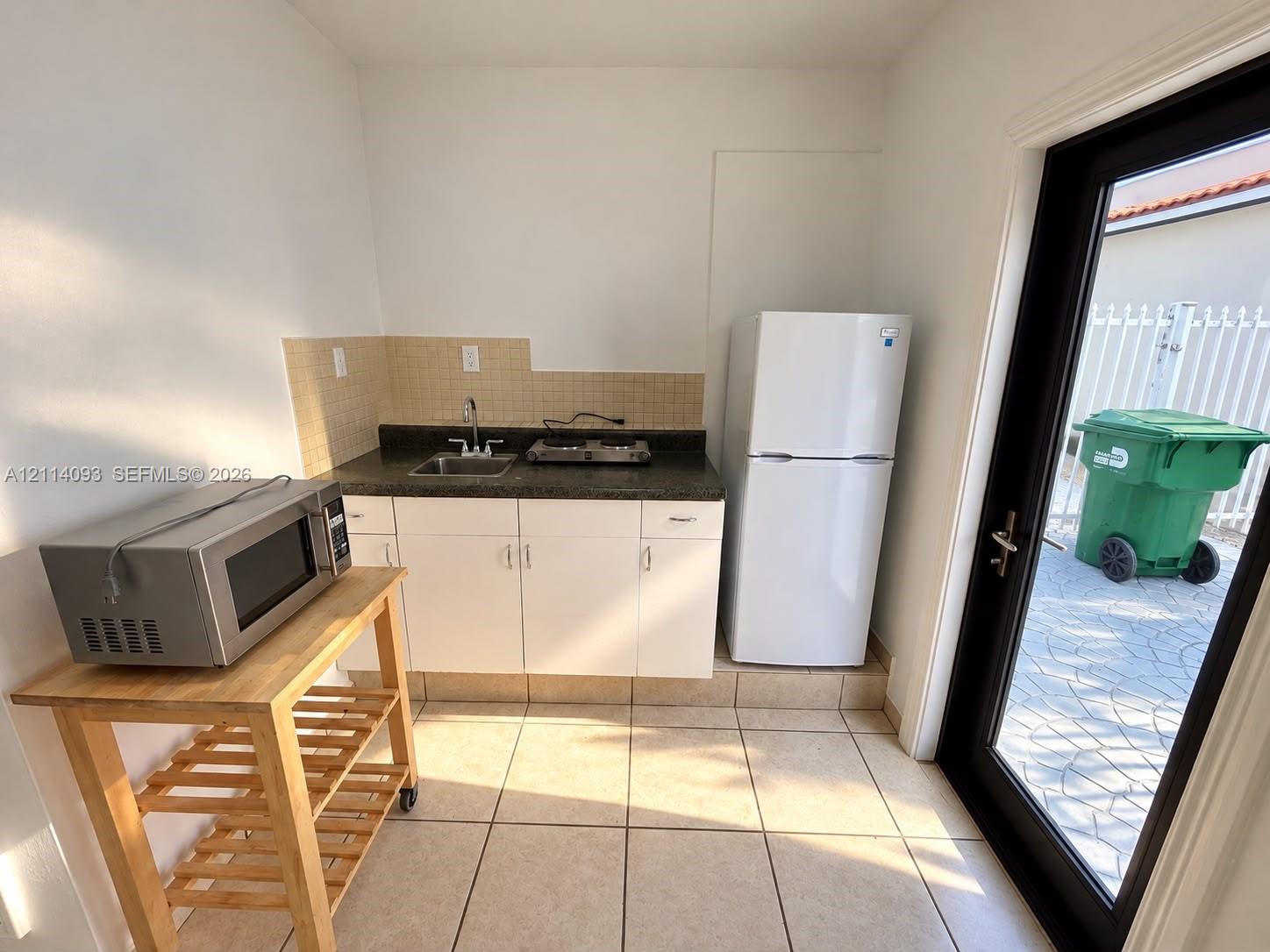 Kitchenette featuring white cabinetry, dark stone-finish countertops, tile backsplash, and ceramic floor tiling