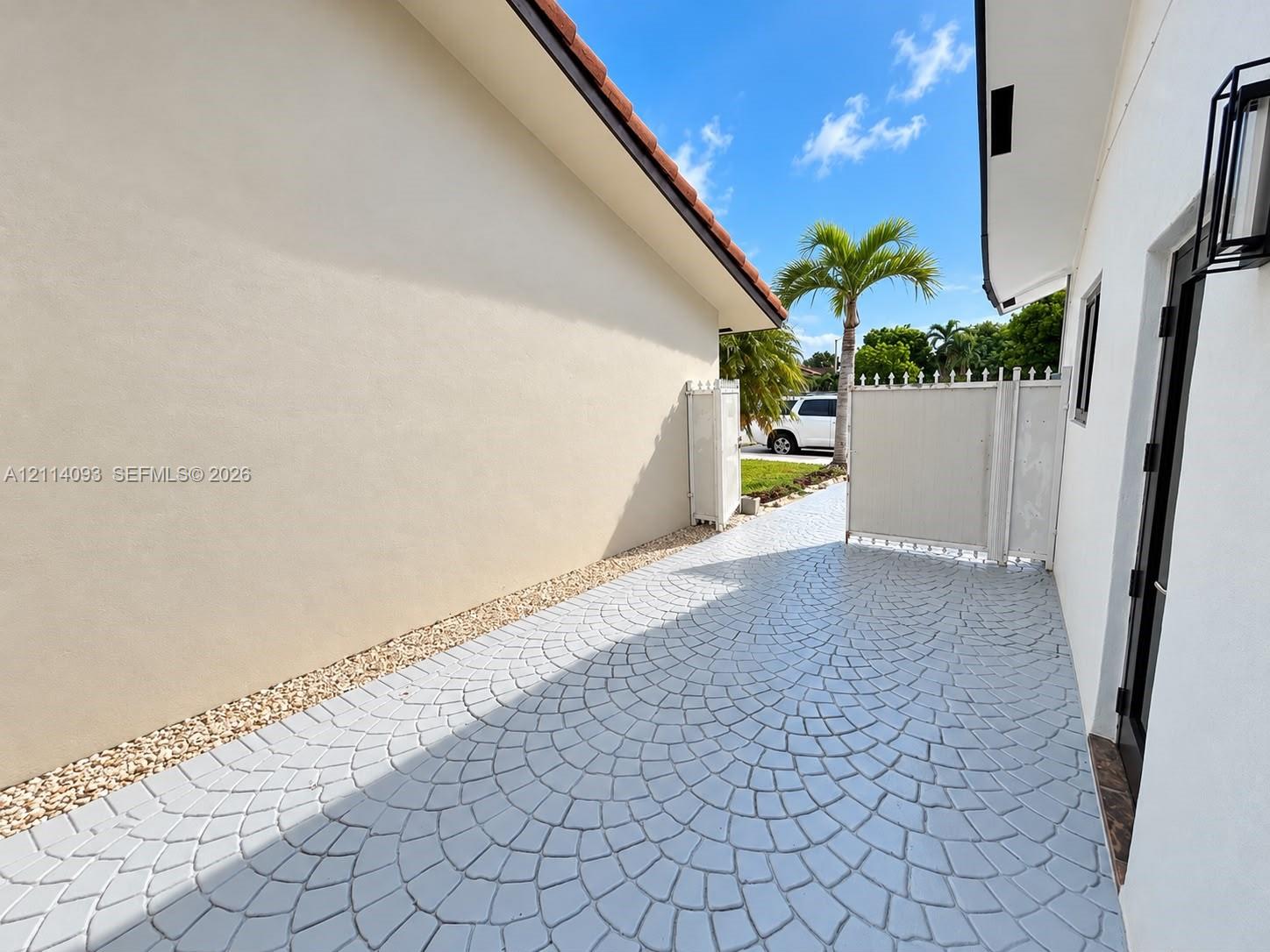 Side exterior featuring stamped concrete patio, light-colored stucco siding, gravel ground cover, and a white privacy gate