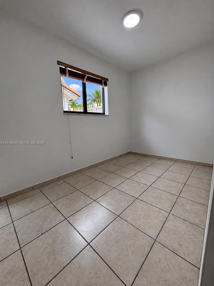 Neutral-toned tile flooring, white wall finishes, flush-mount ceiling lighting, and a single-pane window with a wooden valance