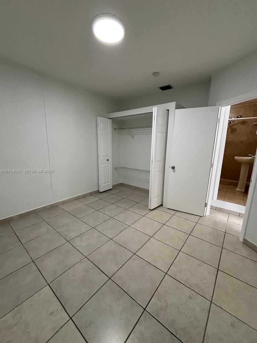 Neutral-toned ceramic tile flooring, built-in closet with shelving, and flush-mount ceiling lighting