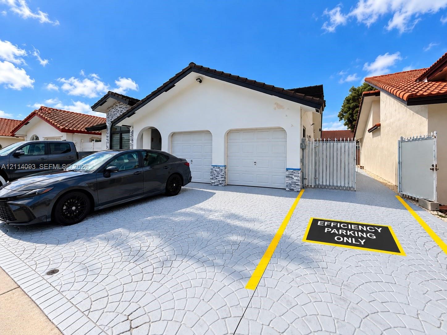 Stucco exterior featuring a two-car garage, patterned concrete driveway, stone facade accents, and a metal privacy gate