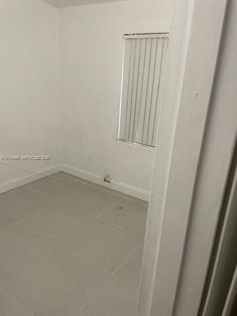 Neutral interior room featuring large-format tile flooring, white wall finishes, and a single window with vertical blinds