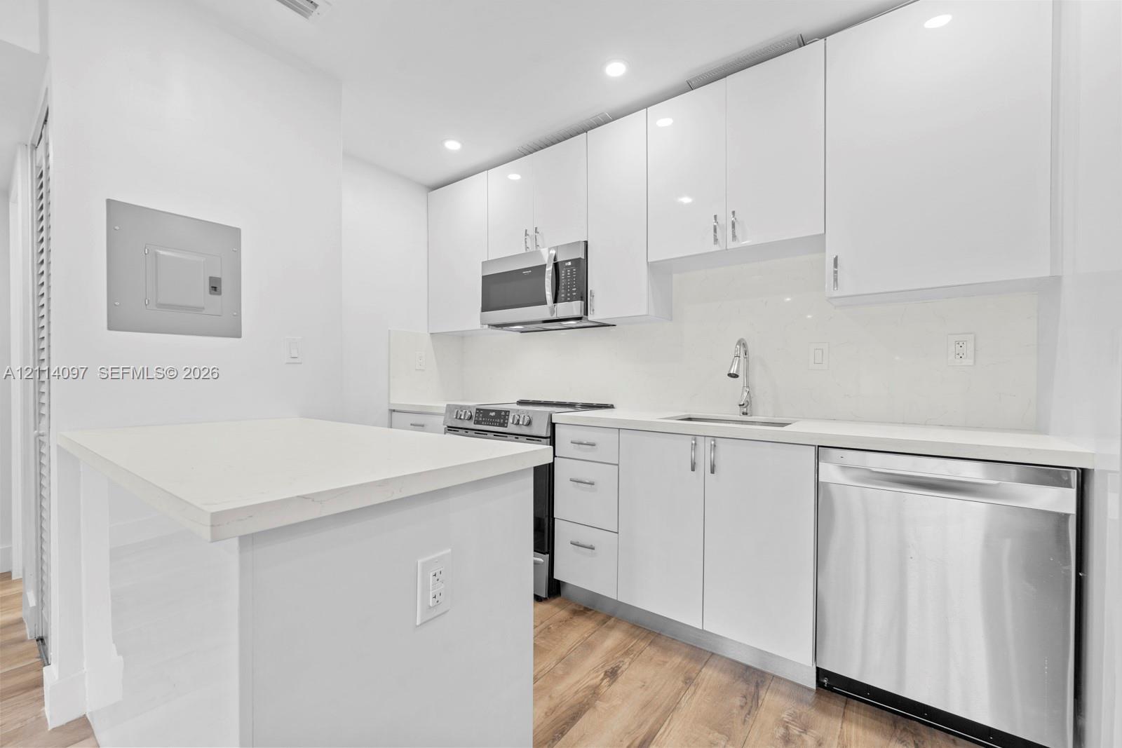 Kitchen featuring white high-gloss cabinetry, stainless steel appliances, white solid-surface countertops, wood-finish flooring, and recessed ceiling lighting
