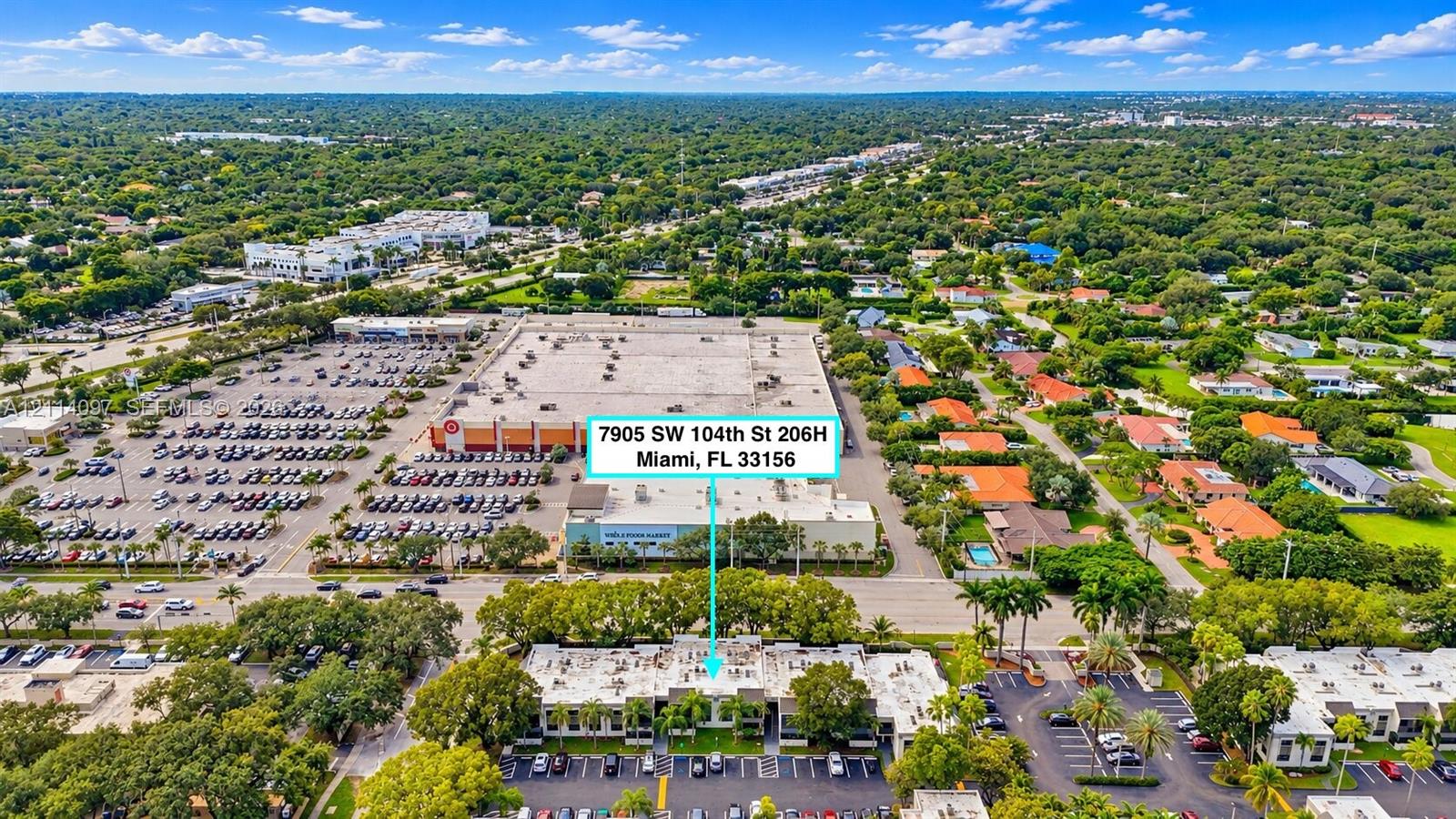 Aerial perspective of a multi-unit complex featuring exterior parking areas, low-rise architecture, and mature trees situated in a developed urban area