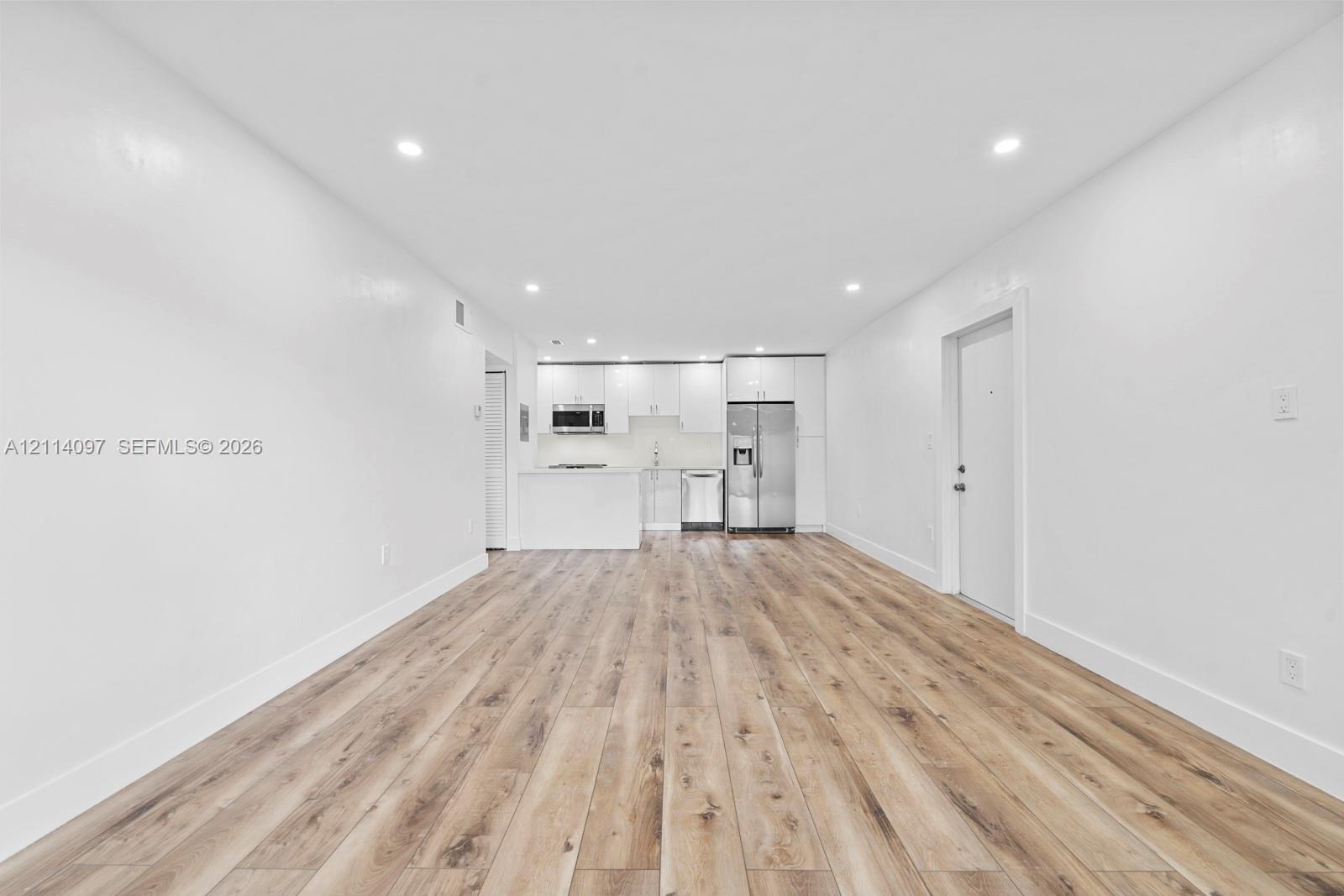 Open-concept interior featuring wood-finish flooring, recessed lighting, and a kitchen equipped with stainless steel appliances, white cabinetry, and a peninsula