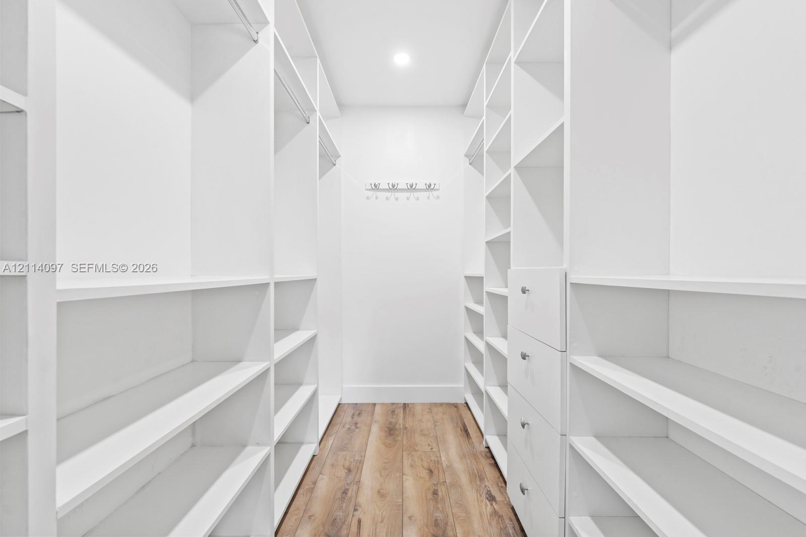 Walk-in closet featuring white built-in shelving, integrated garment rods, custom drawer storage, and wood-finish flooring