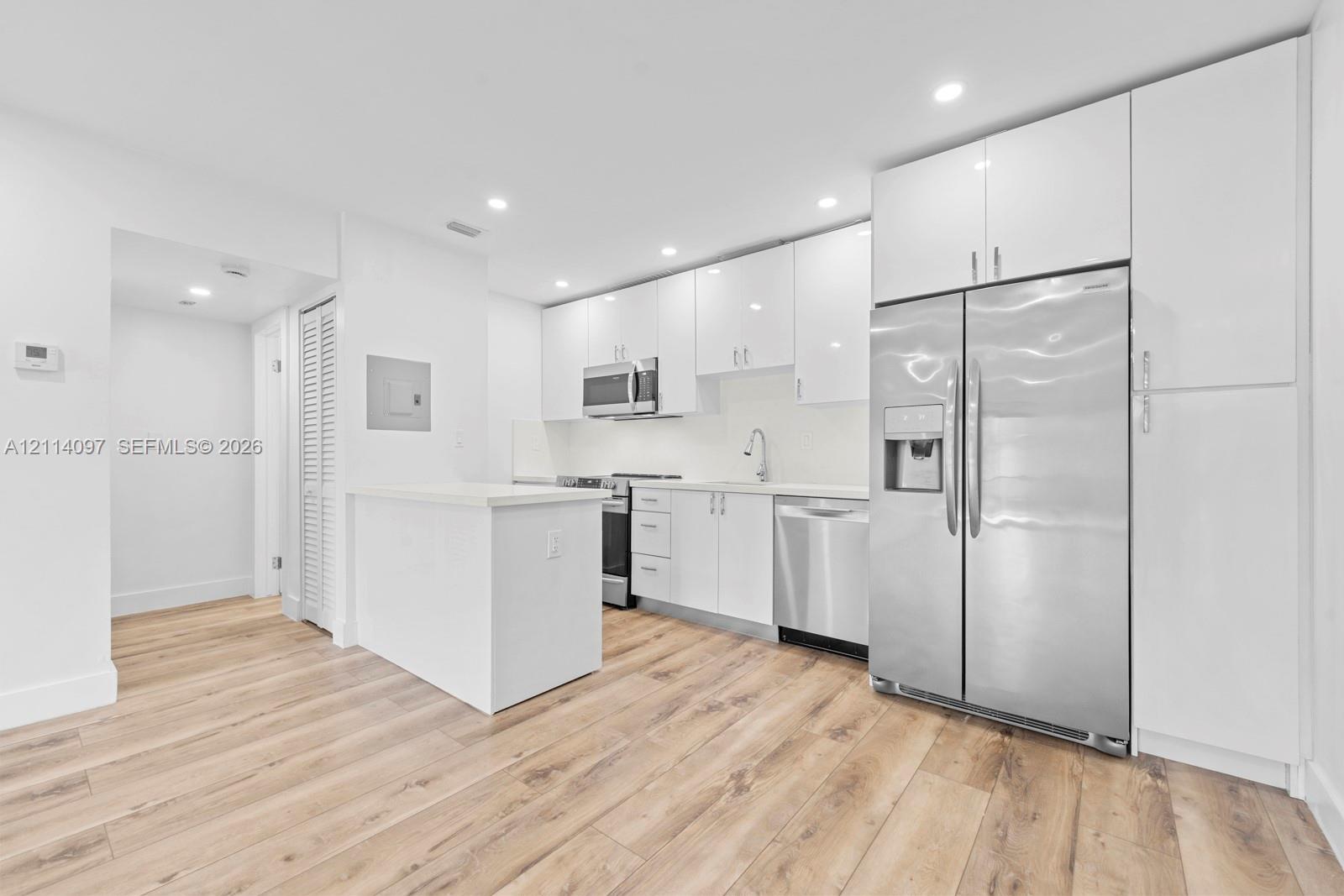 Kitchen featuring white high-gloss cabinetry, stainless steel appliances, wood-finish flooring, quartz countertops, and recessed lighting
