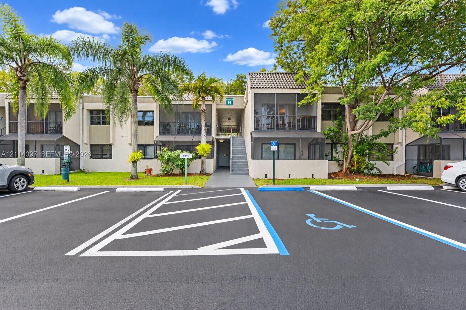 Two-story exterior featuring a neutral stucco facade, tile roofing, screened-in balconies, and mature landscaping