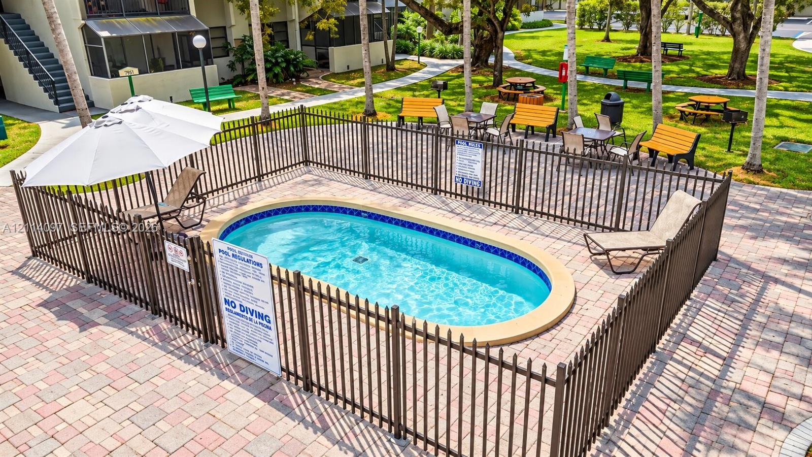 Oval swimming pool featuring a decorative tile border, surround fencing, and a paver stone deck