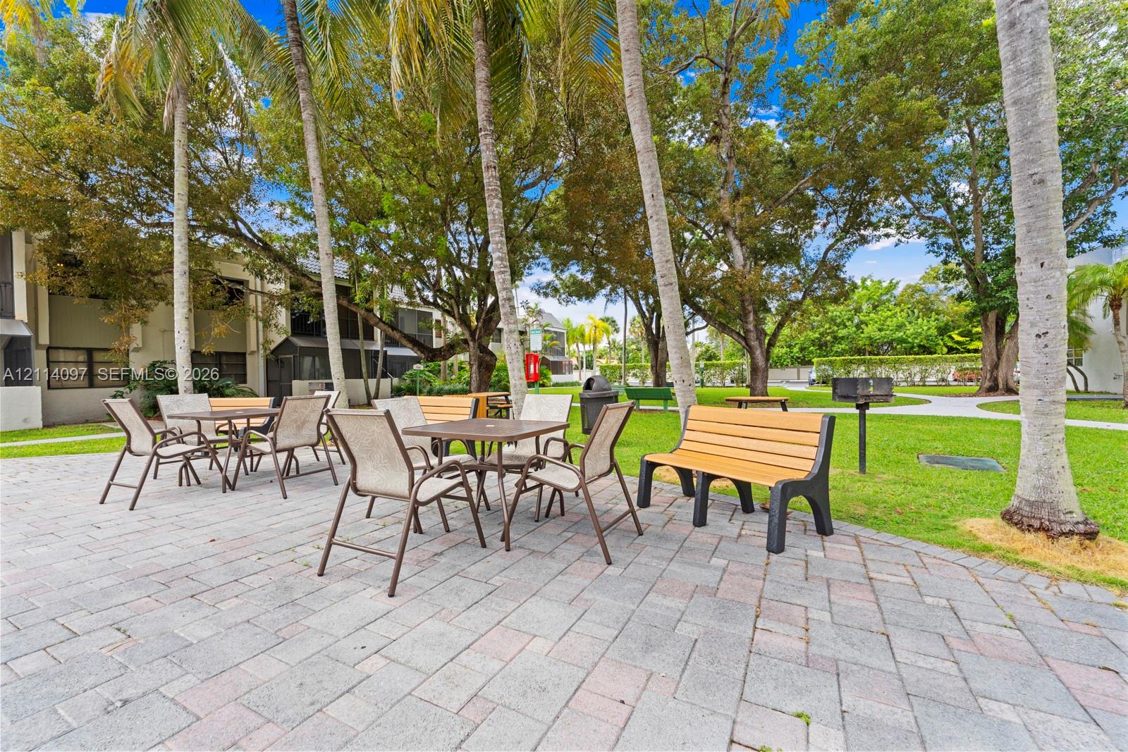 Outdoor recreation area featuring a paved stone patio, built-in pedestal grill, and mature palms set within a landscaped lawn
