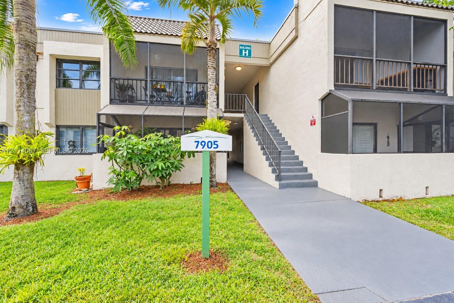 Multi-level stucco exterior featuring screened balconies, covered staircase with metal railing, and paved entry walkway