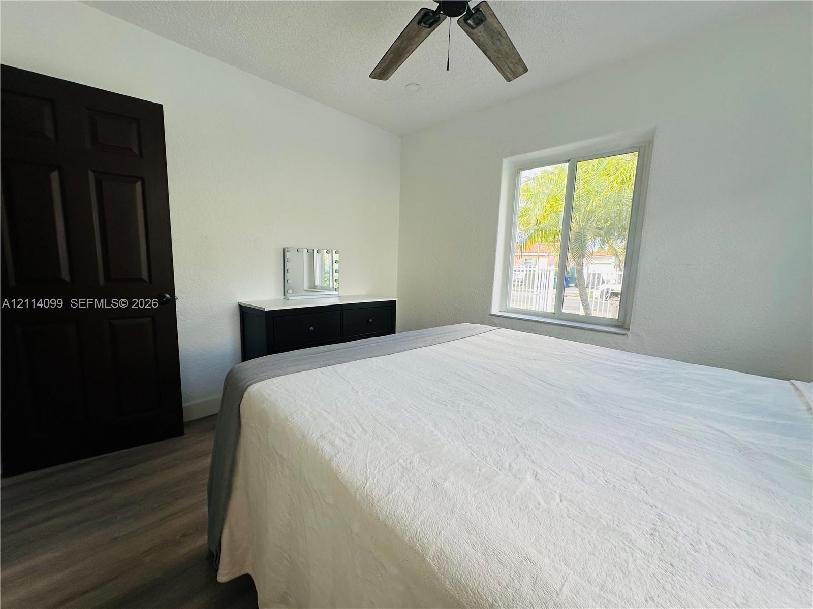 Room featuring wood-finish flooring, a dark-toned solid core door, and a ceiling fan with integrated lighting
