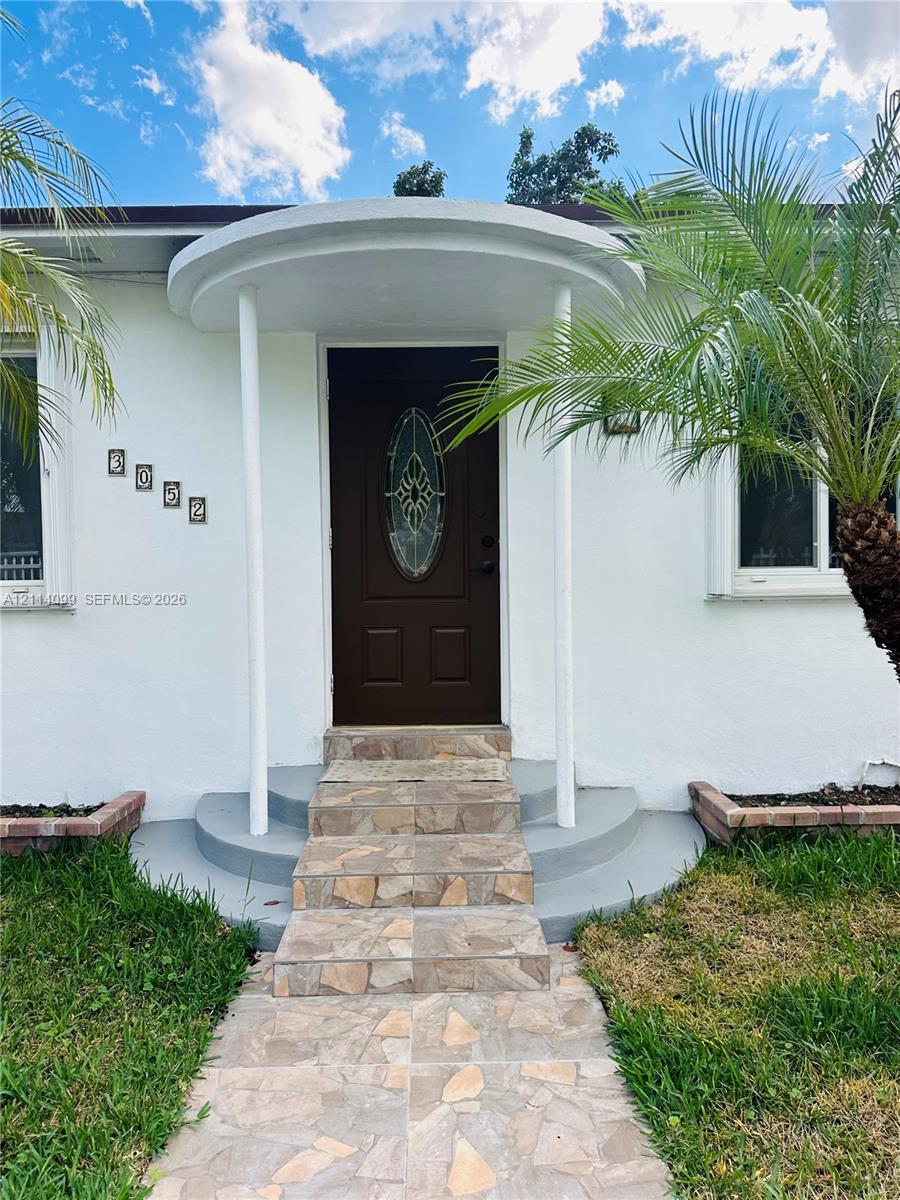 Exterior entrance featuring a covered circular portico with dual structural columns, stone-tile walkway and steps, and a solid-panel door with an oval glass insert
