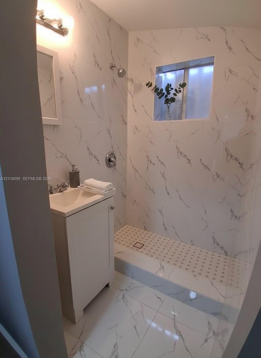 Full-height wall tiling with a veined pattern, walk-in shower with a low-profile threshold, high-gloss floor tiling, vanity cabinet with a integrated sink, and wall-mounted vanity lighting