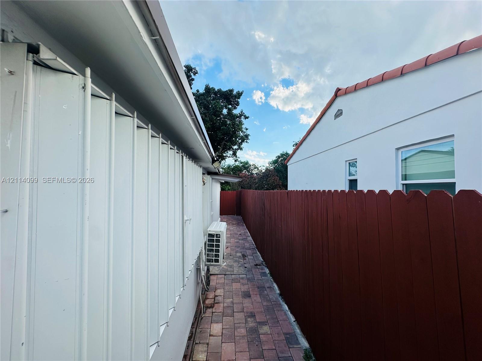 Exterior side walkway featuring brick paver flooring, vertical siding, and a wood privacy fence