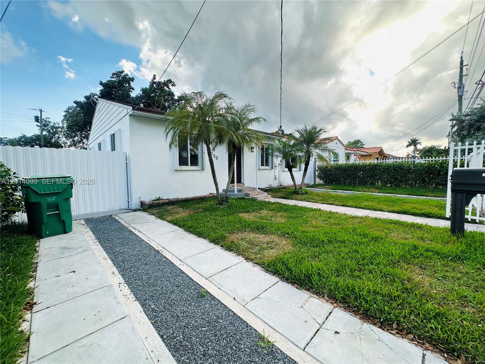 Single-story exterior with white siding, dual-material paved driveway, and perimeter white fencing