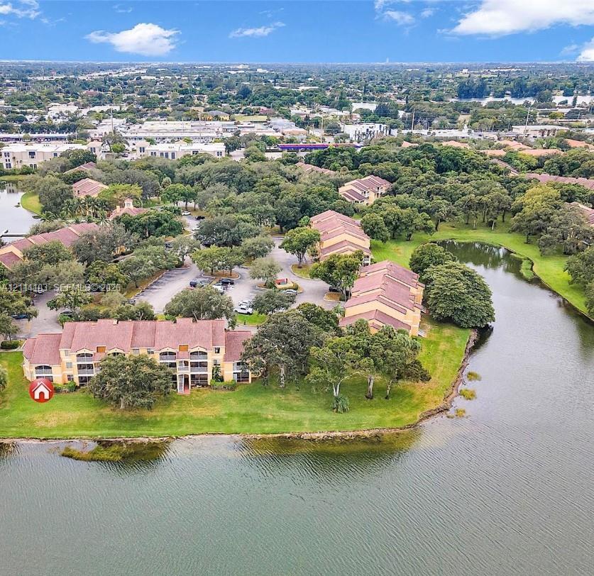 Multi-story residential buildings featuring tile roofs, private balconies, paved parking areas, and expansive water frontage surrounded by mature trees