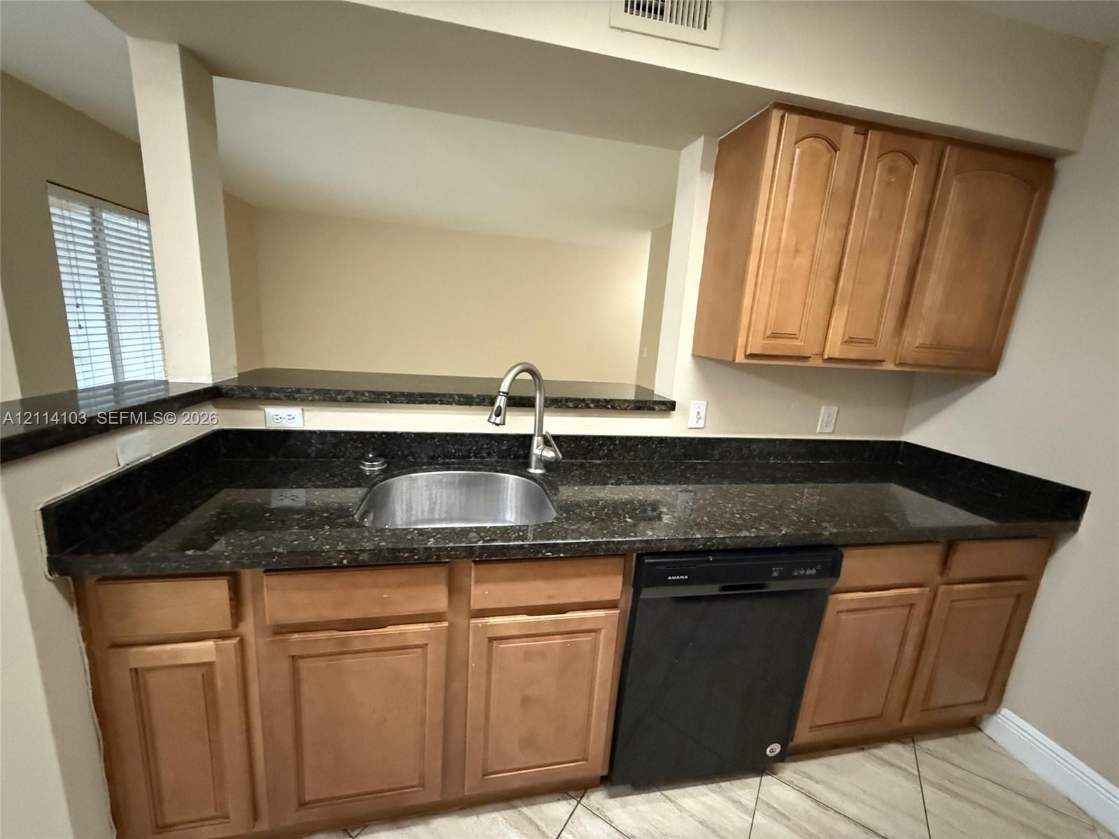 Kitchen area featuring dark stone countertops, natural wood-finish cabinetry, a stainless steel undermount sink with a gooseneck faucet, and a black built-in dishwasher