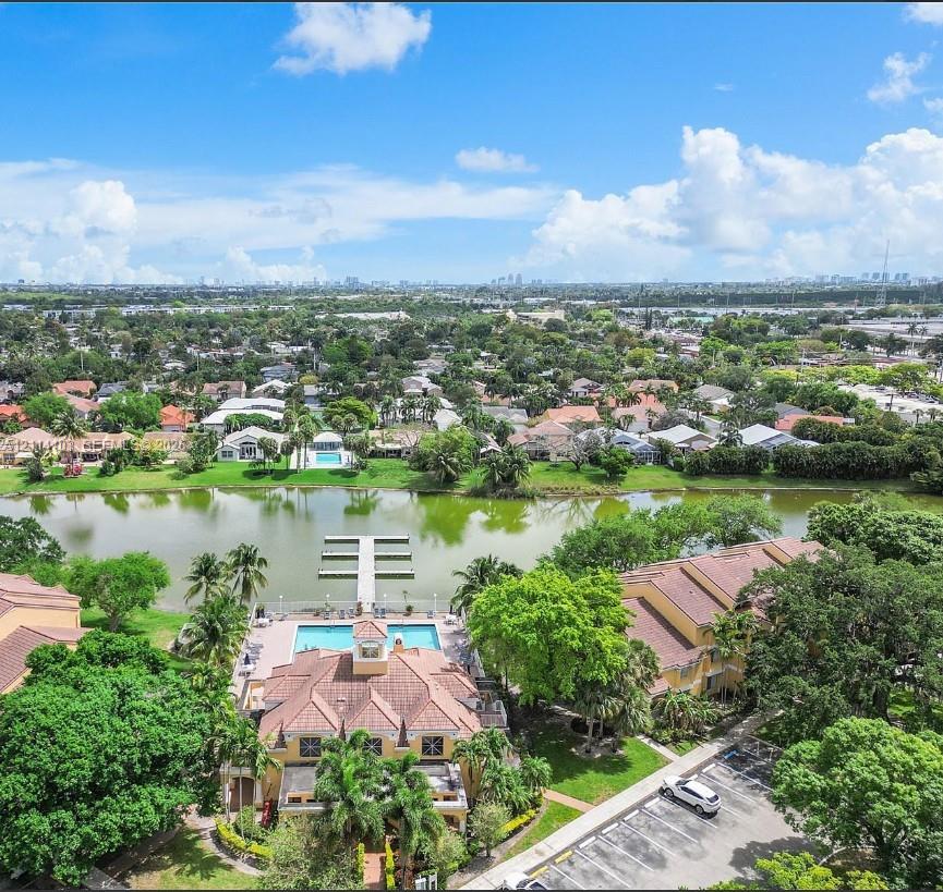 Aerial perspective of property grounds featuring a swimming pool, a private dock extending into the lake, a multi-story structure with a tiled roof, and mature landscaping