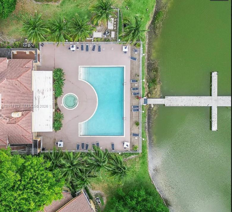 Aerial perspective of an expansive pool deck featuring a geometric swimming pool, integrated spa, tiled patio, and private boat dock extending into the water