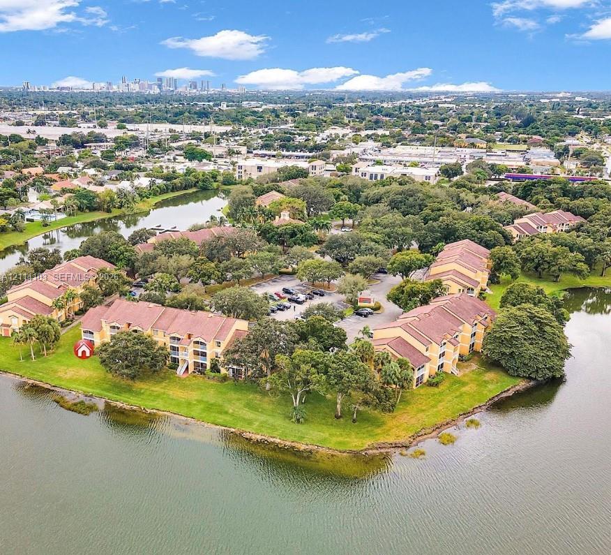 Multi-story residential complex featuring barrel-tile roofs, exterior balconies, expansive waterfront positioning, mature landscaping, and central surface parking