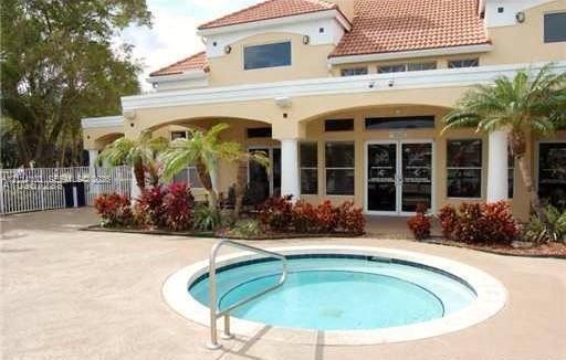 In-ground spa with a metal handrail, concrete deck, covered patio, stucco exterior, and multi-pitched tile roof