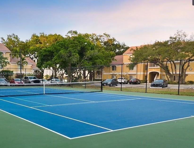 Tennis court with blue and green court surfacing, perimeter chain-link fencing, and white court markings