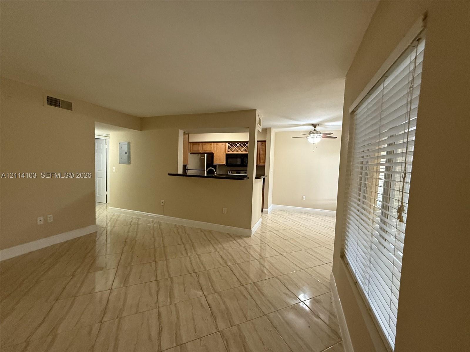 Open-concept interior featuring large-format tile flooring, a pass-through kitchen opening with a breakfast bar, wood cabinetry, and a ceiling fan