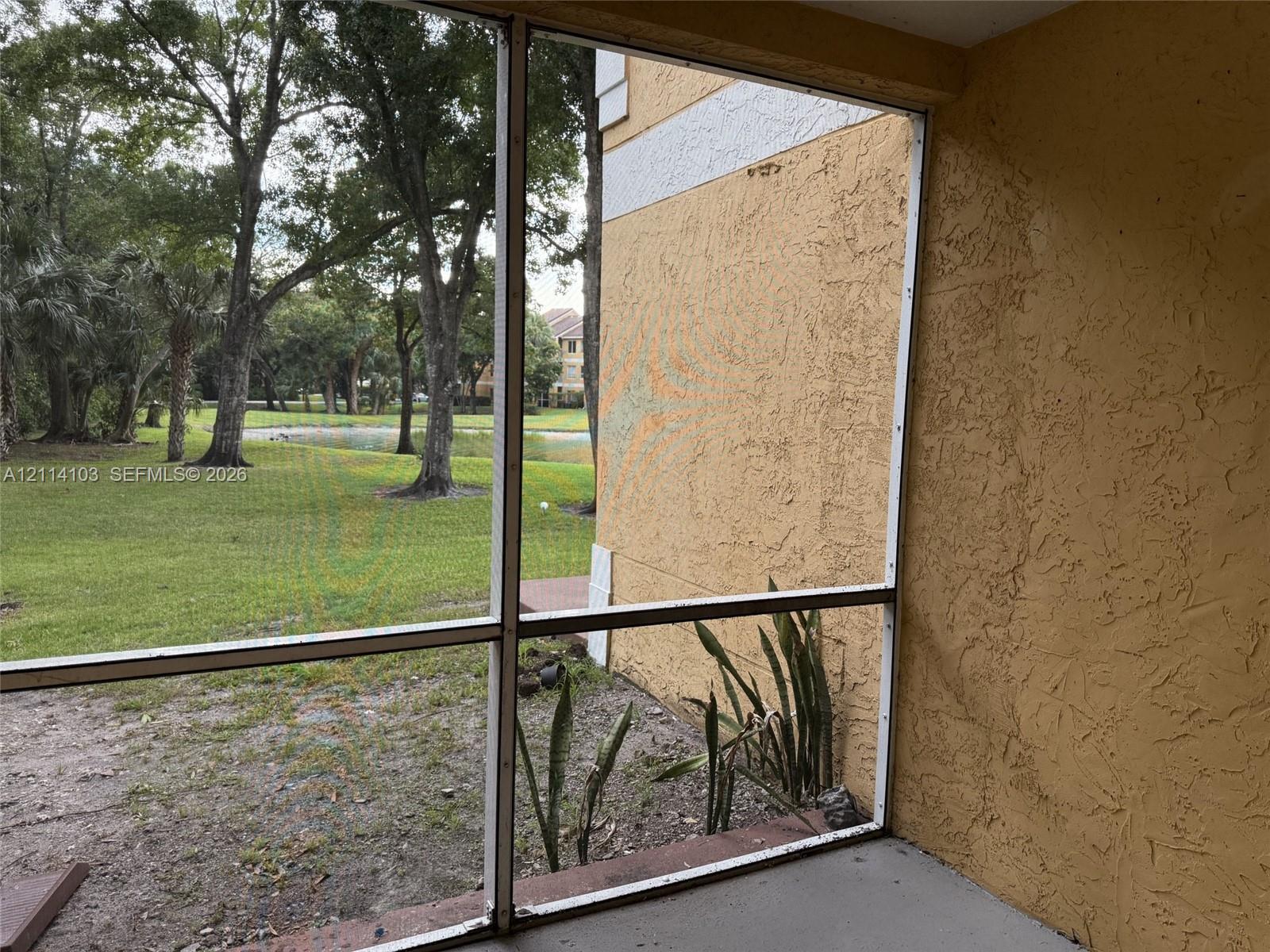 Screened-in porch featuring a concrete floor, textured stucco exterior wall, and an outdoor area with mature trees and a pond