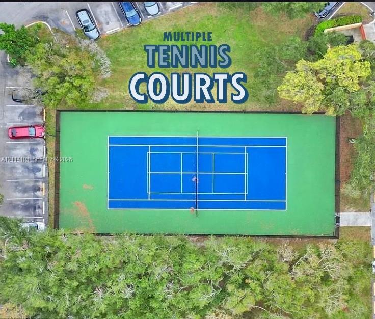 Tennis court featuring a multi-color surface, perimeter fencing, and surrounding mature trees