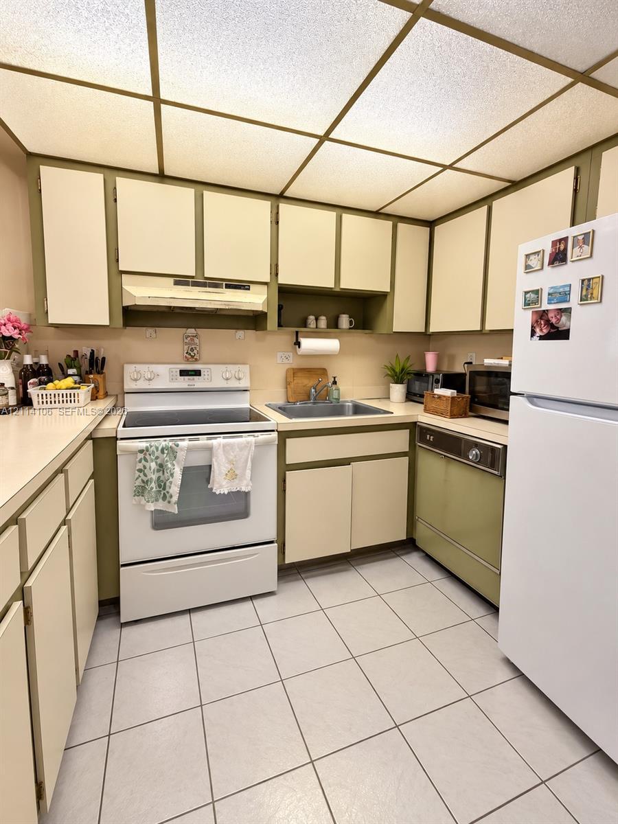 Kitchen featuring flat-panel cabinetry, a dual-basin stainless steel sink, a drop-ceiling grid with integrated lighting, and ceramic tile flooring
