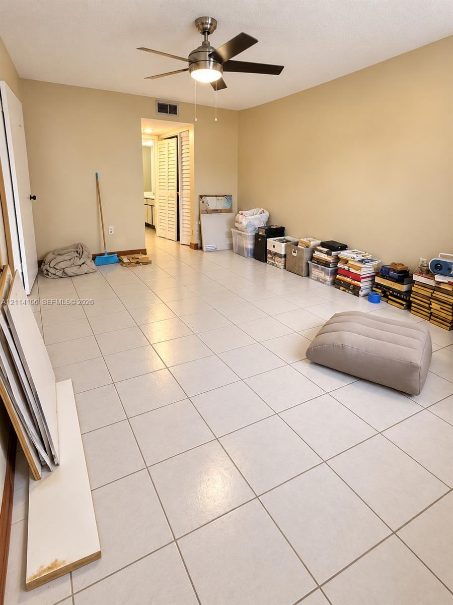 Neutral-toned interior space featuring light-colored square tile flooring and a ceiling-mounted light fixture with a five-blade fan
