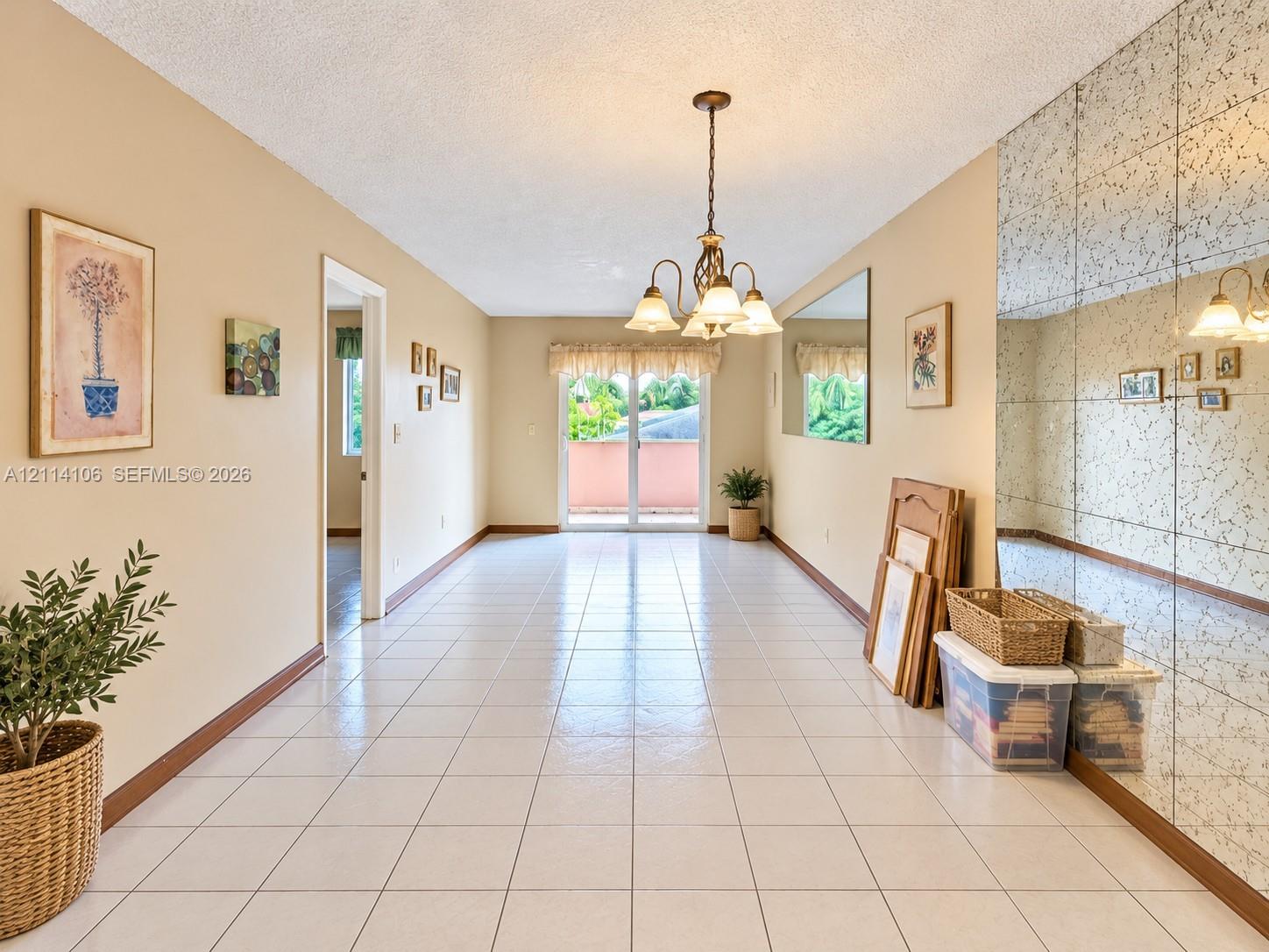 Light-filled interior featuring neutral tile flooring, an ornate five-light chandelier, a full-wall mirrored accent, and sliding glass doors providing outdoor access