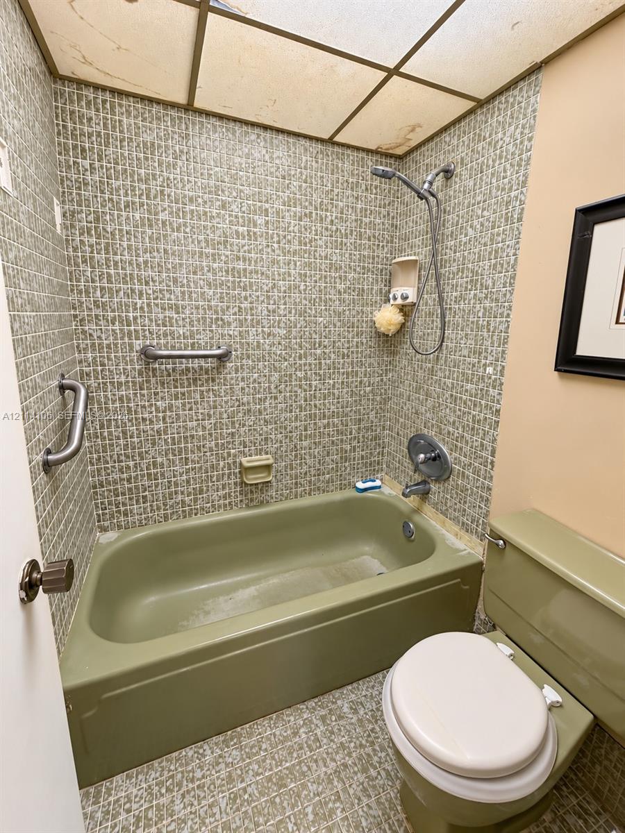 Bathtub and shower combination featuring a handheld showerhead, grid-pattern wall tiling, and dual metal grab bars