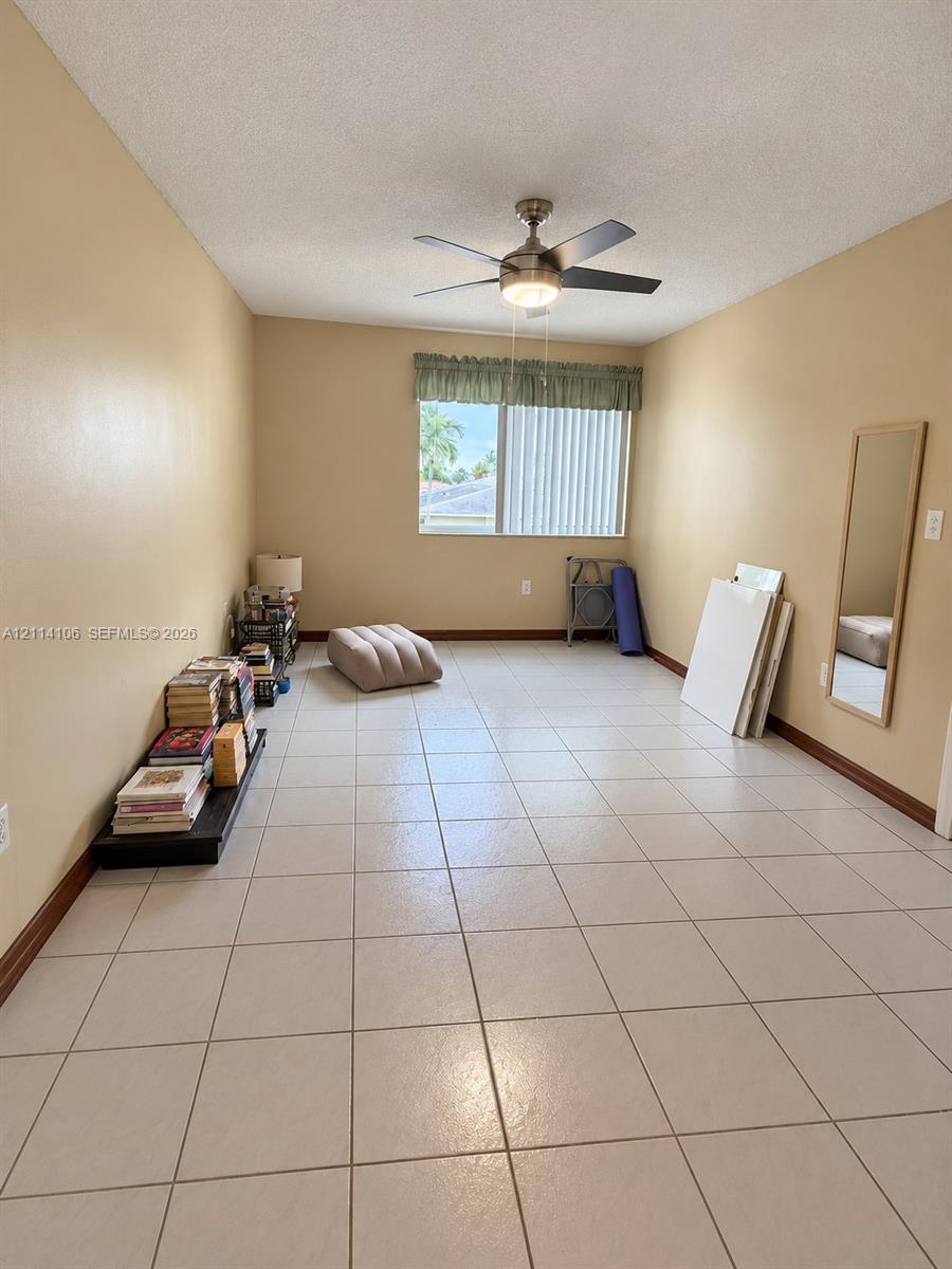 Neutral-toned interior featuring large-format ceramic tile flooring, a polished metal ceiling fan with integrated lighting, and a window with a fabric valance and vertical blinds