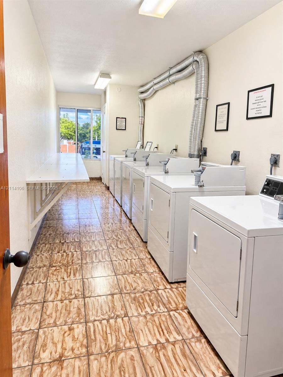 Utility room featuring neutral tile flooring, a wall-mounted folding counter, and multiple built-in laundry appliances