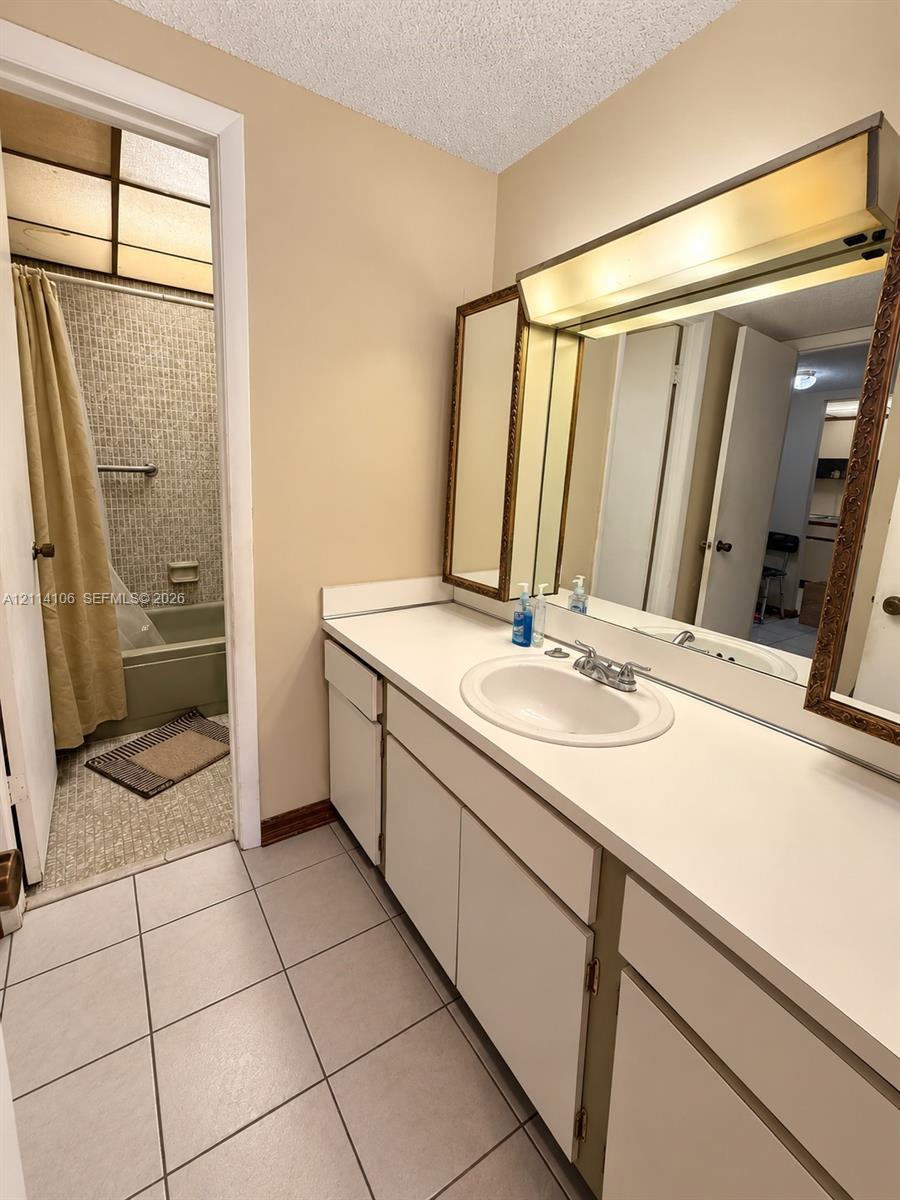 Bathroom featuring a vanity with an integrated basin, a tri-panel mirror with integrated lighting, tiled flooring, and a tub-shower combination with full-height tile surround