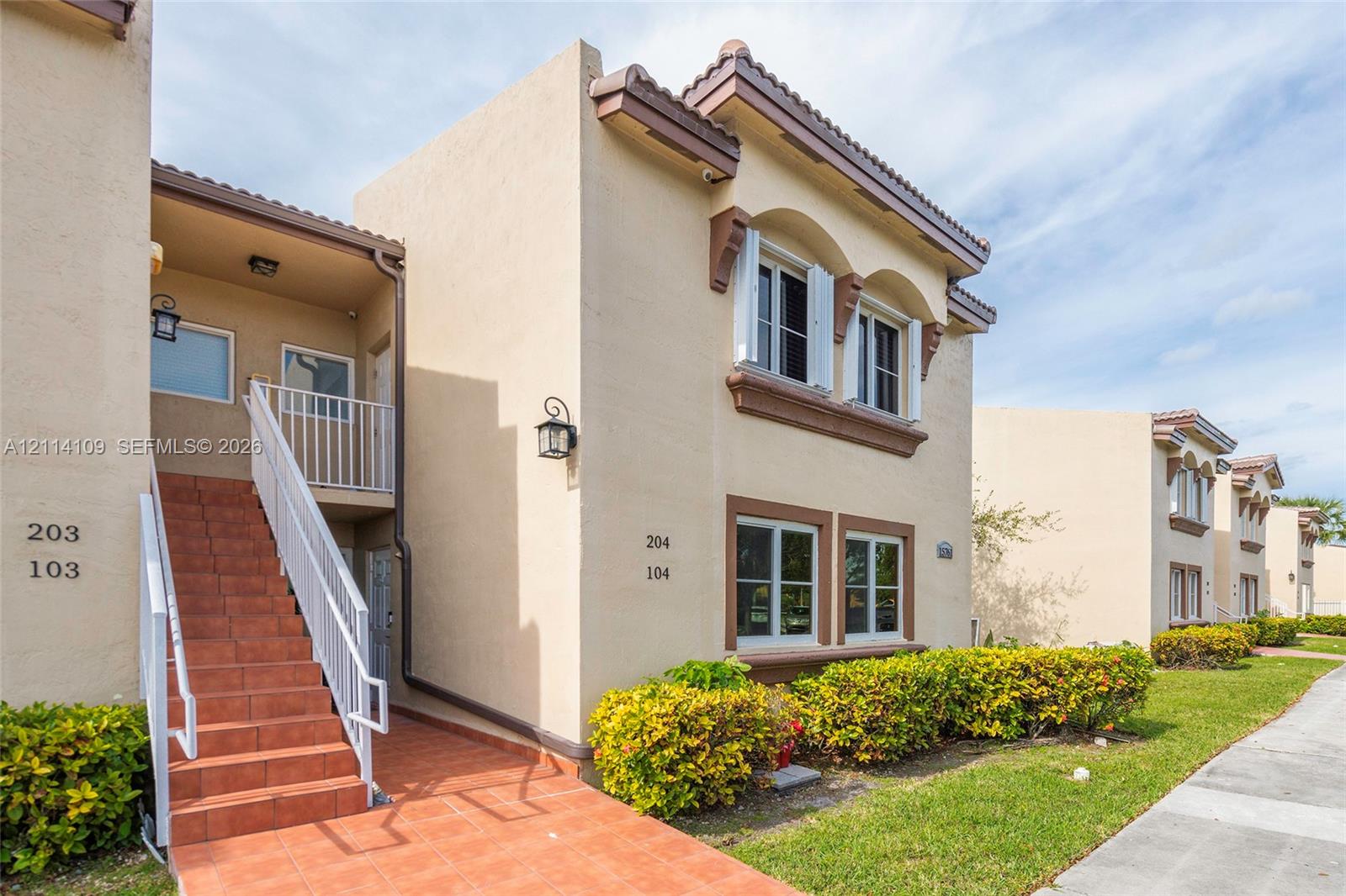 Stucco exterior featuring arched window details, terracotta-tiled staircase, metal railings, and attached wall-mounted lantern-style lighting