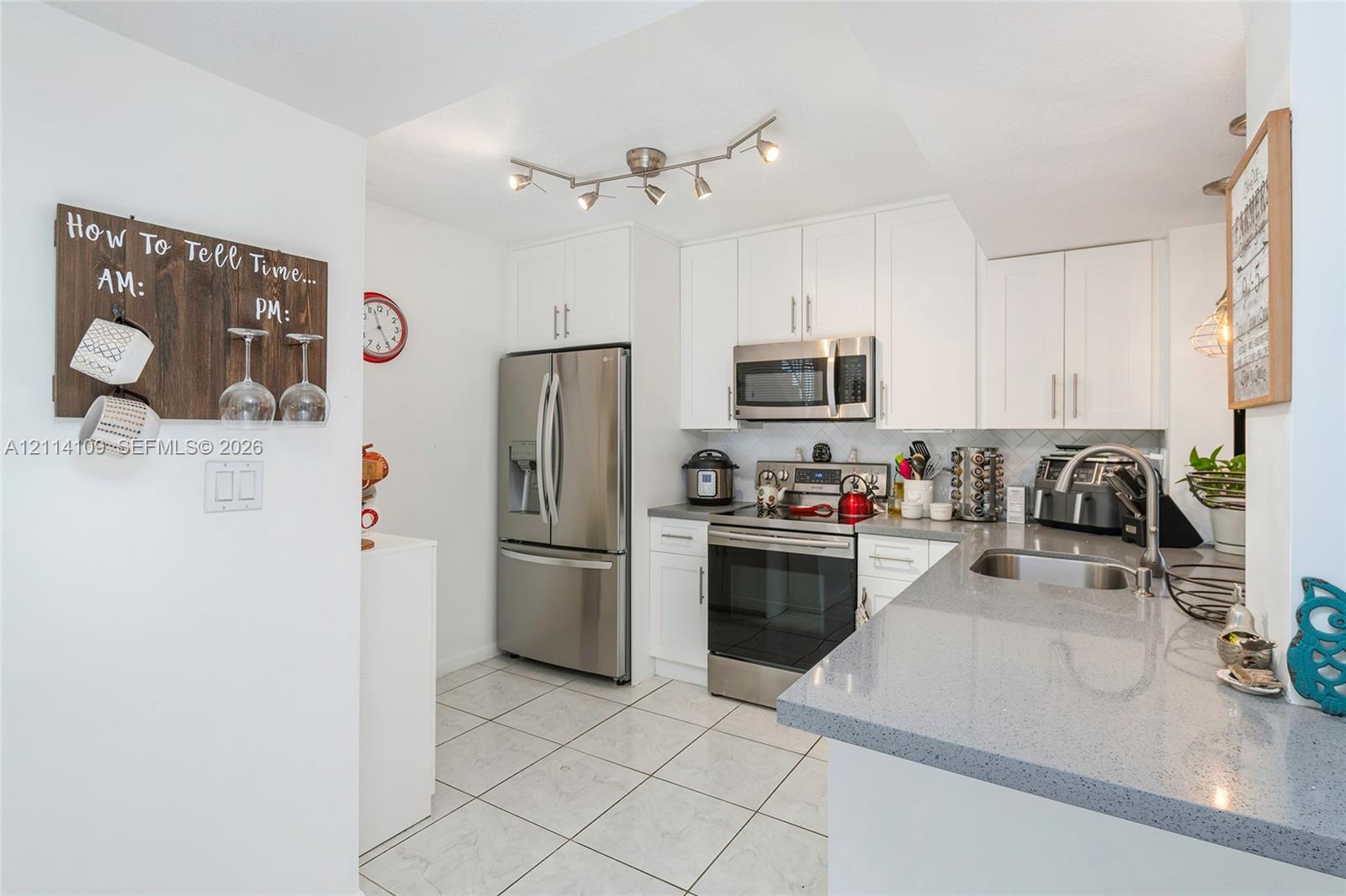 Kitchen featuring white cabinetry, solid surface countertops, stainless steel appliances, multi-directional track lighting, and tile flooring