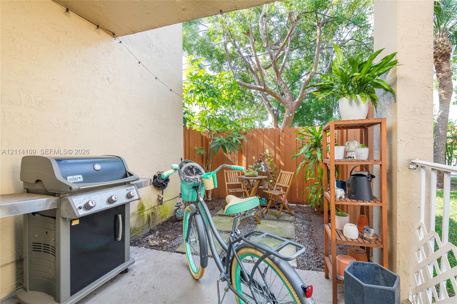Covered concrete patio featuring a perimeter wood privacy fence, stone paver accents, and mature tree landscaping