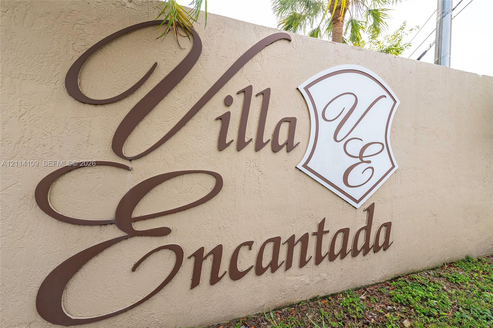 Stucco monument sign featuring raised, metallic-finish lettering and a decorative shield emblem