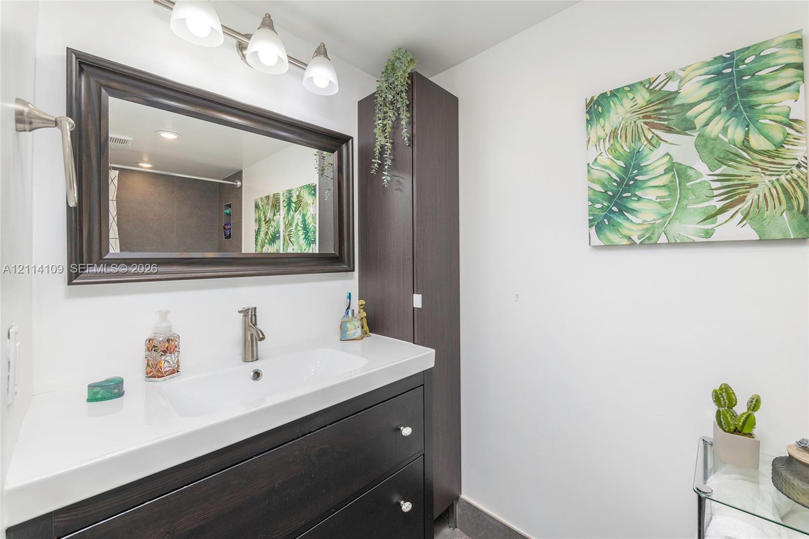 Bathroom vanity featuring dark wood-finish cabinetry, white countertop, integrated rectangular sink, brushed nickel faucet, and matching framed mirror with three-light fixture
