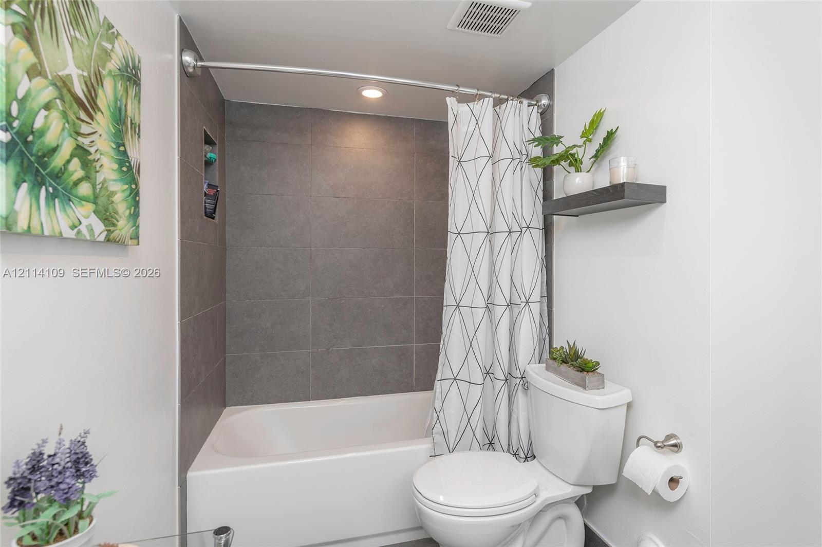 Bathroom featuring a soaking tub, floor-to-ceiling charcoal tile surround, integrated shower niche, and a wall-mounted floating shelf