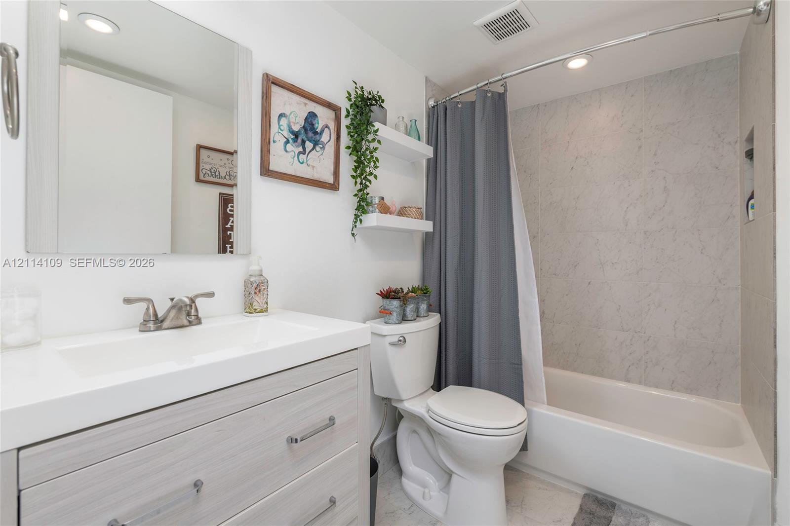 Bathroom featuring a vanity with a white countertop and integrated sink, recessed lighting, wall-mounted shelving, and a tub-shower combination with full-height stone-patterned wall surround and integrated niche