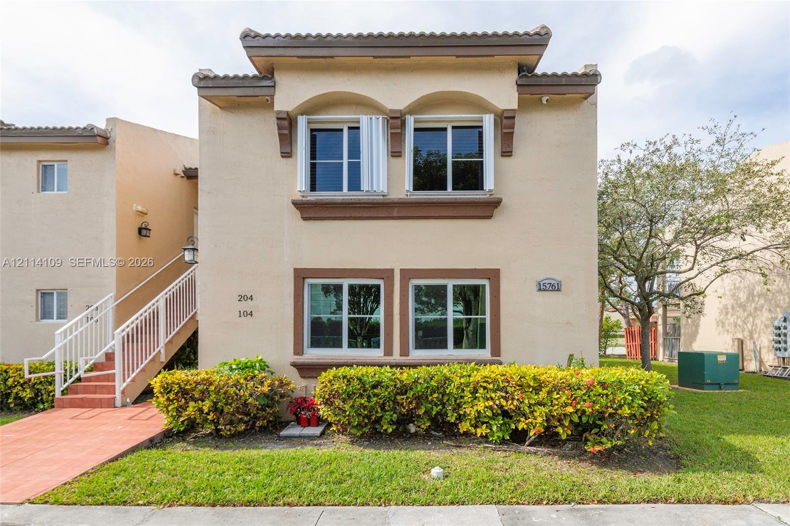 Stucco exterior featuring dual-level arched window accents, tile roof trim, and an exterior staircase with white metal railings