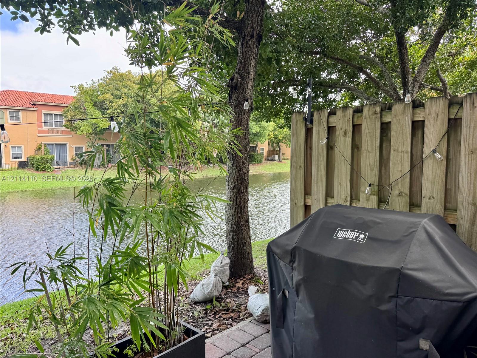 Waterfront patio featuring paver hardscaping, mature trees, and a wooden privacy fence